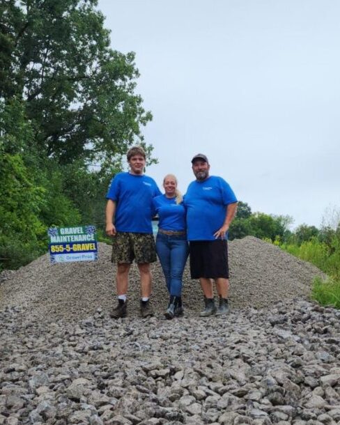 Three people standing on a gravel road holding up a sign.